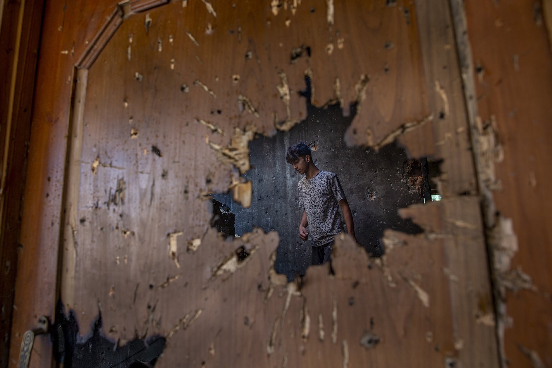 A man inspecting a house where suspected Kashmiri militants had taken refuge, is seen through a hole created by a mortar shell fired by government forces during a gunfight, in Srinagar, Indian-administered Kashmir. Officials said two suspected militants were killed in the gunfight.